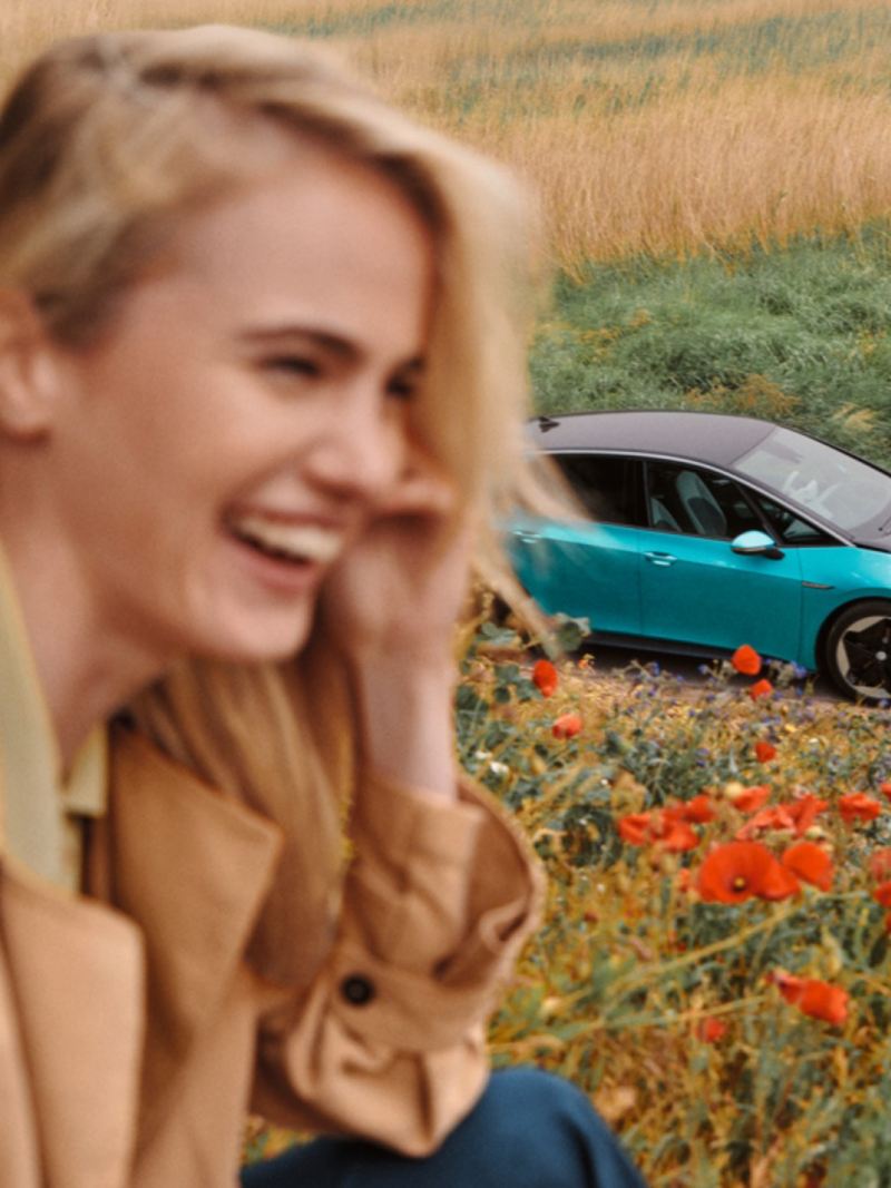 Chica en primer plano sonriendo en un campo de flores delante de un Volkswagen ID.3