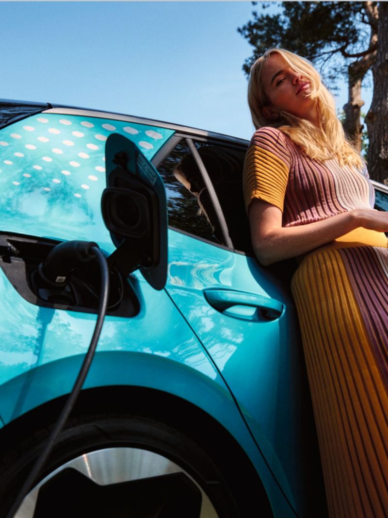 Chica apoyada en un Volkswagen ID.3 con el cargador conectado