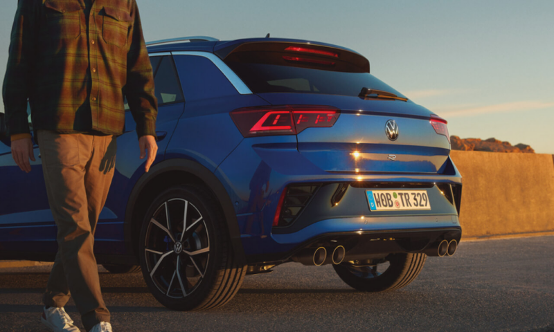 Chico caminando al lado de un Volkswagen T-Roc R azul colocado en diagonal.