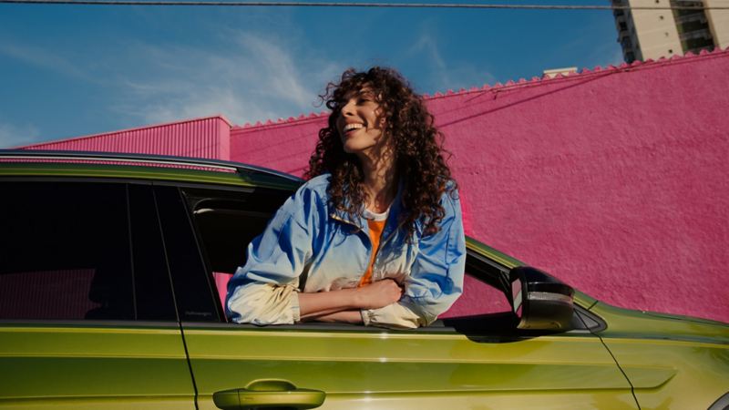 Chica sonriendo asomándose por la ventanilla de un Volkswagen SUV verde