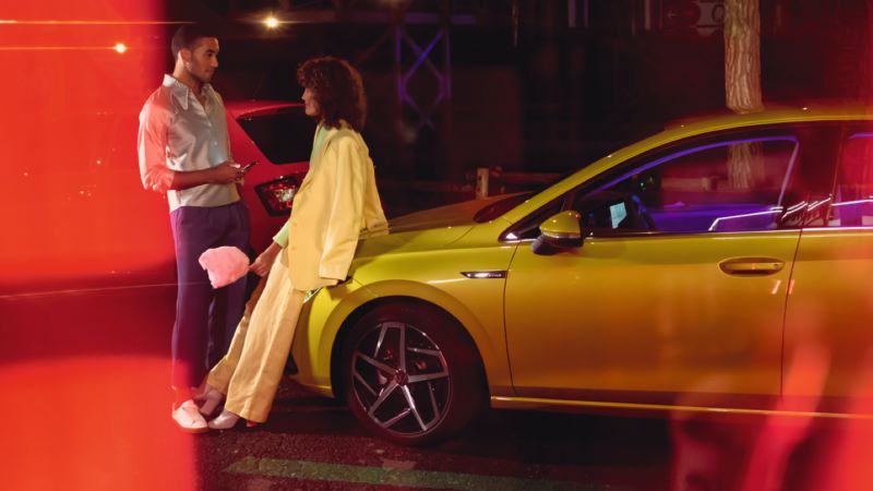 Una pareja hablando delante de un Volkswagen Golf 8 amarillo