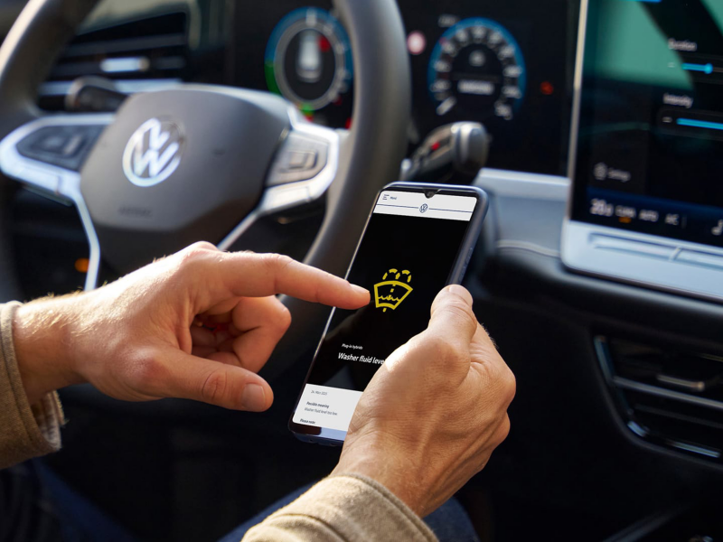 Un hombre sentado en un Volkswagen revisando el significado de las luces de advertencia en el móvil