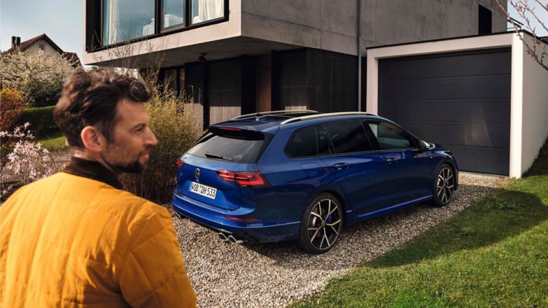 Un hombre delante de un Volkswagen Golf Variant R azul aparcado delante de casa
