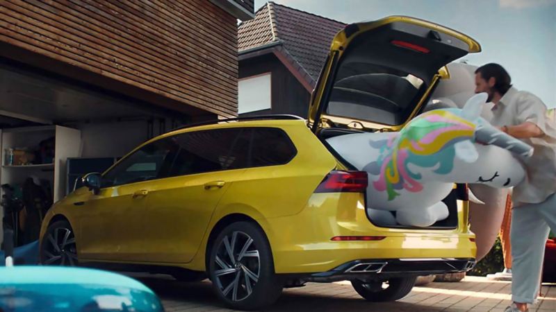 Un hombre metiendo un juguete inflable en el maletero de un Volkswagen Golf 8 Variant amarillo