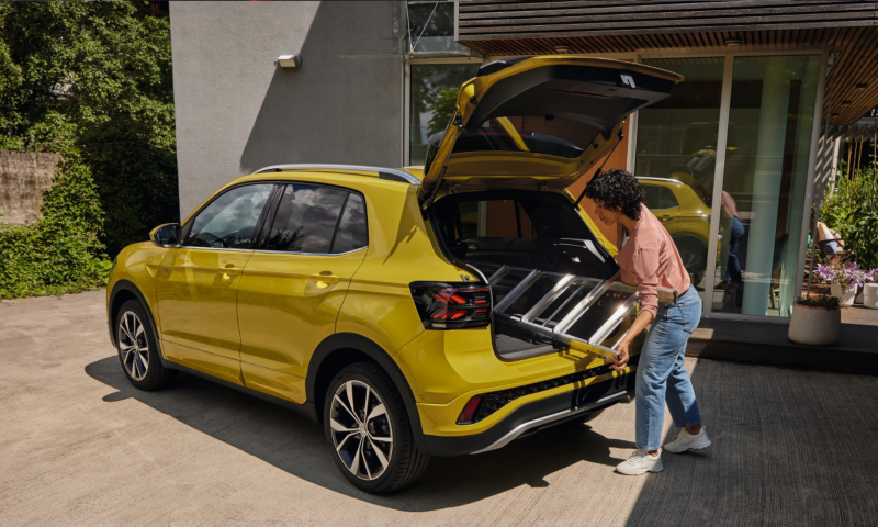 Una chica introduciendo una escalera en el maletero de un Volkswagen T-Cross de color amarillo