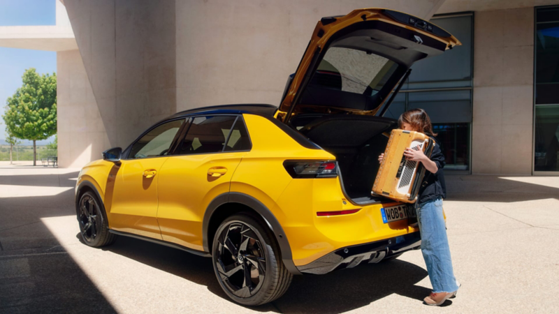 Una chica poniendo una caja en el maletero de un Volkswagen de color amarillo
