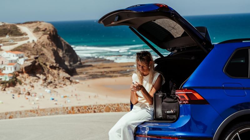 Chica sentada dentro del maletero de un Volkswagen T-Roc R delante de la playa