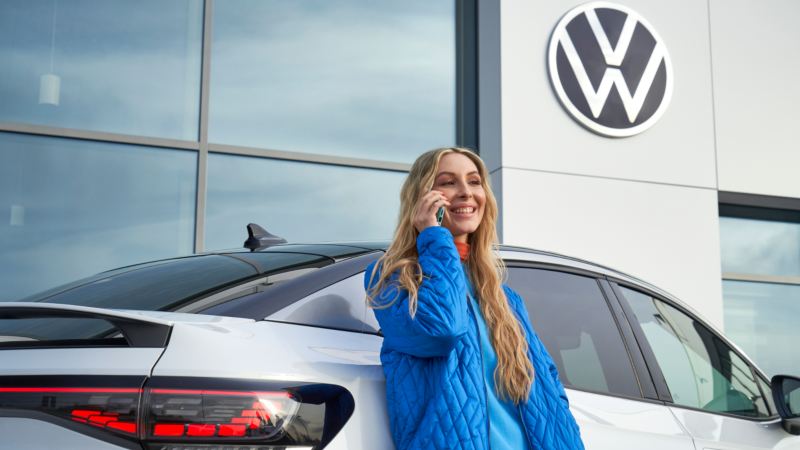 Una mujer hablando por móvil delante de un coche Volkswagen