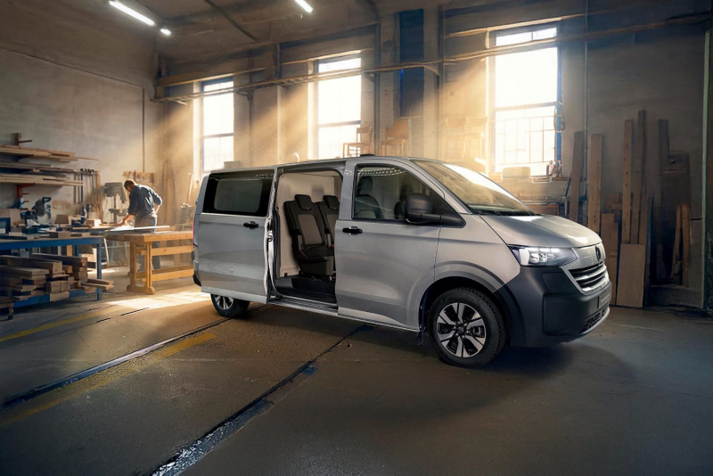 Una trabajadora autónoma cargando postes de madera en la plataforma de carga del VW Transporter furgón.