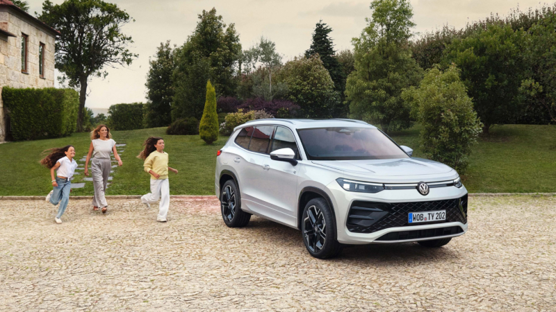 Una madre con dos niñas corriendo hacia un Volkswagen de la Gama SUV de color blanco