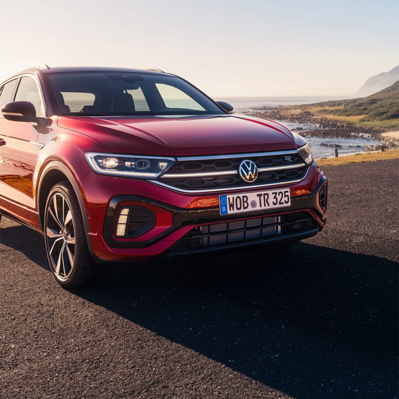 Detalle frontal Volkswagen T-Roc rojo con una playa detrás