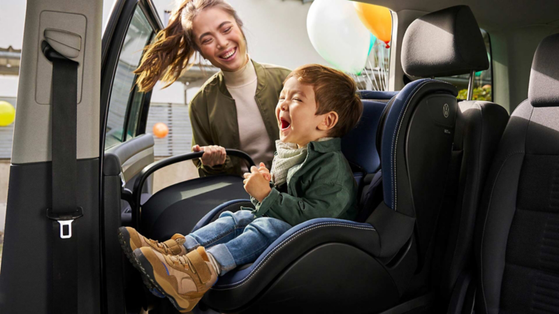 Una mujer riendo junto a un niño sentado en la sillita dentro de un Volkswagen Touran