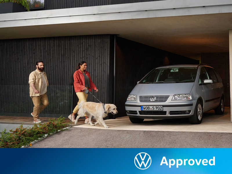 Una pareja un con un perro junto a un Volkswagen Sharan estacionado en un parking