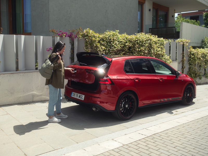 Una chica abriendo el maletero de un Volkswagen Golf de color rojo estacionado en la calle