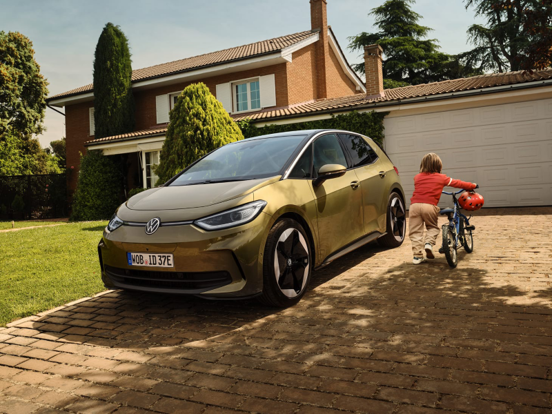 Un chico arrastrando una bici de espaldas junto un Volkswagen ID.3 amarillo aparcado frente al garage de una casa
