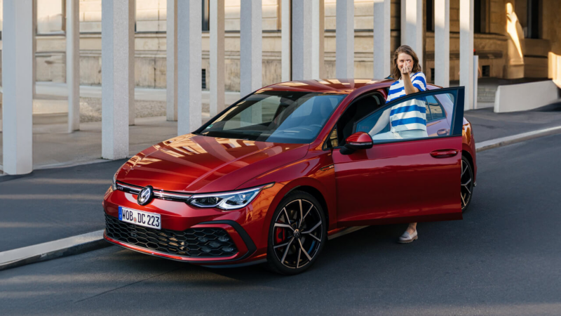 Una chica en la puerta de un Volkswagen Golf de color rojo