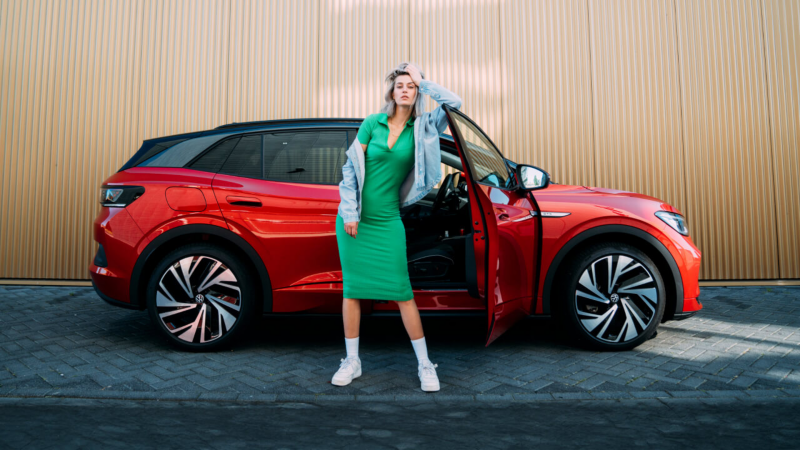 Una chica apoyada en la ventada de un Volkswagen ID.4 GTX de color rojo