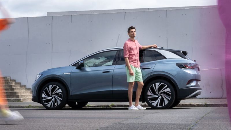 Un chico al lado de un Volkswagen ID.4 de color azul estacionado en la calle