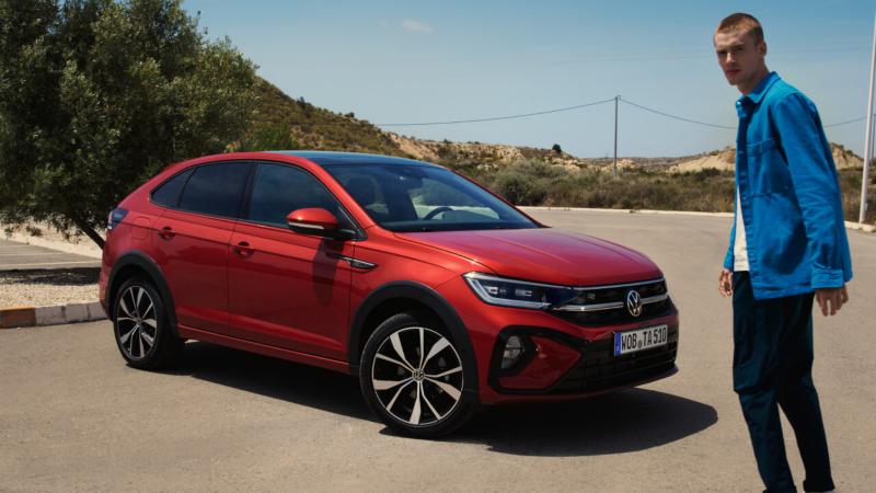 Un chico delante de un Volkswagen Taigo de color rojo estacionado en la calle