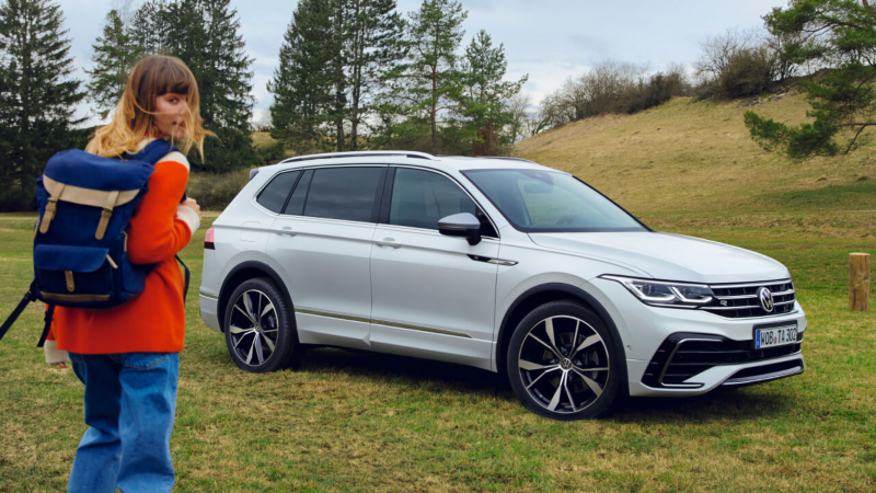 Una chica delante de un Volkswagen Tiguan Allspace de color blanco estacionado en el campo