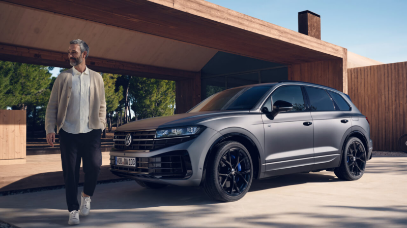 Un hombre delante de un Volkswagen Touareg R de color gris estacionado fuera de una casa