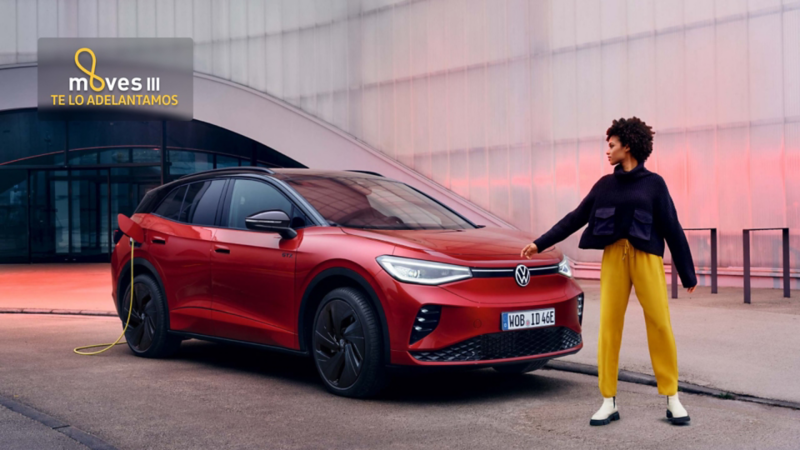 Una mujer al lado de un Volkswagen de color rojo estacionado en la calla y conectado a carga