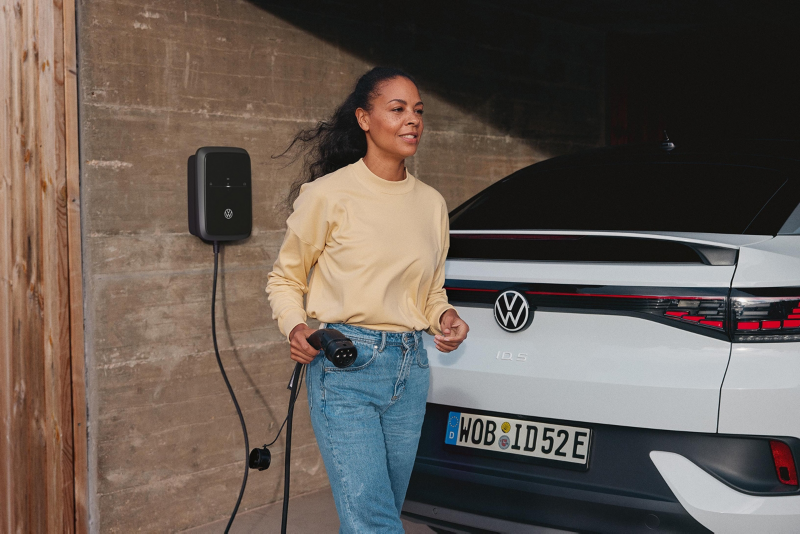 Una chica sujetando el cable de carga de un Volkswagen eléctrico