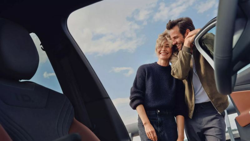 Una pareja sonriendo vistos desde el interior de un Volkswagen con la puerta abierta