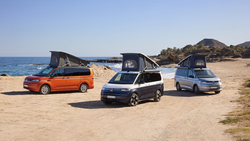 Plano de tres furgonetas de Volkswgen comerciales estacionadas delante de una playa