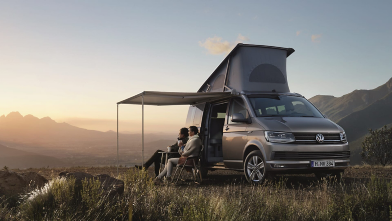Plano furgoneta de Volkswgen comerciales estacionadas en la montaña con una pareja tomando café al atardecer