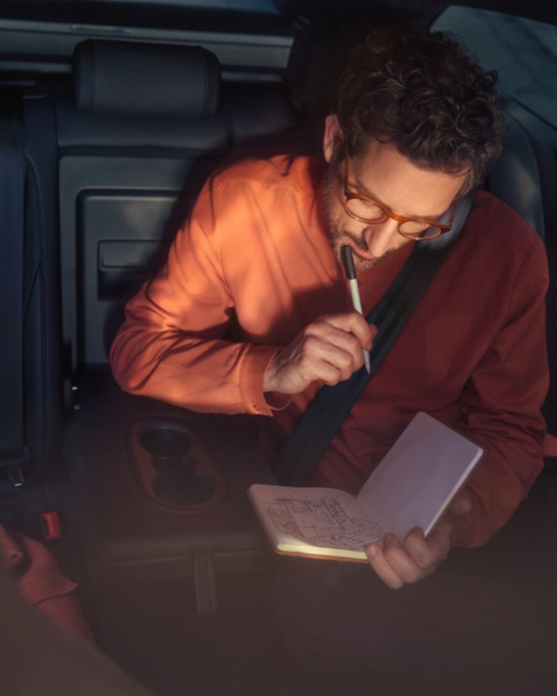 Hombre pensativo escribiendo en una libreta con el bolígrafo en la barbilla