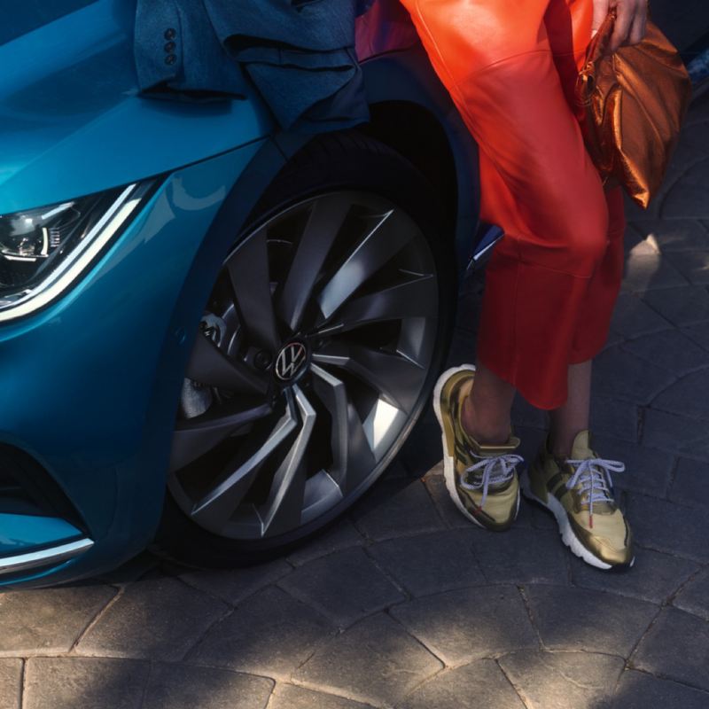 Chica apoyada junto a las ruedas de un Nuevo Volkswagen Arteon azul