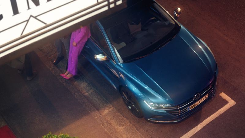 Vista superior de una pareja apoyada en un Nuevo Volkswagen arteon azul con los faros encendidos