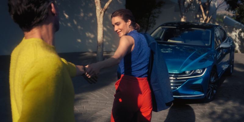Mujer arrastrando de la mano a un hombre hacia un Volkswagen Arteon azul