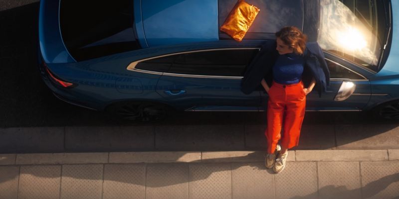 Vista superior de una chica apoyada en un Nuevo Volkswagen azul aparcado en la calle
