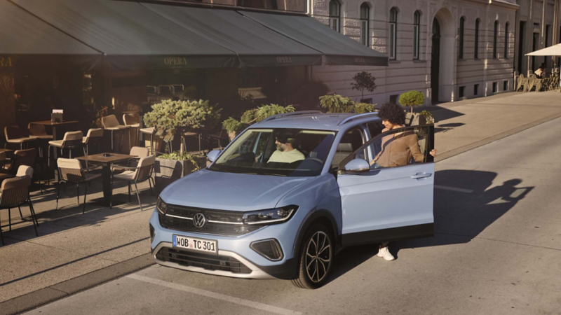 Una mujer subiendo a un Volkswagen T-Cross azul aparcado frente una cafetería