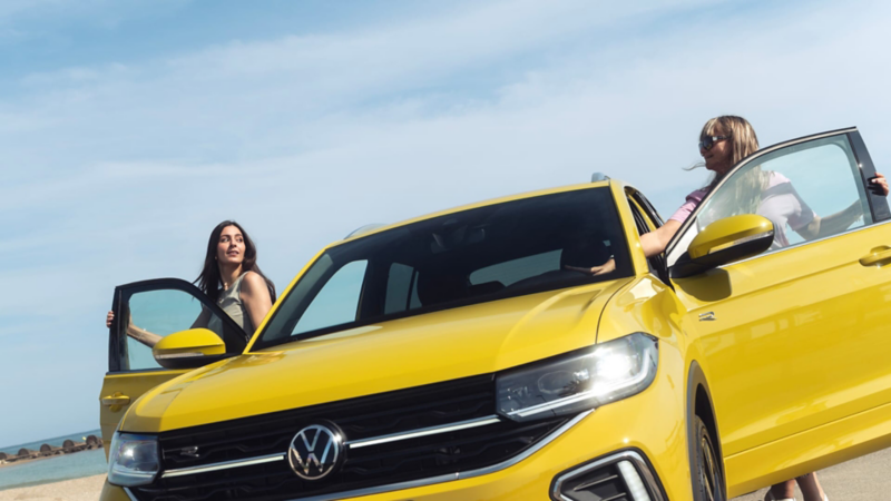 Madre e hija saliendo por las puertas delanteras de Volkswagen T-Cross amarillo estacionado en exterior