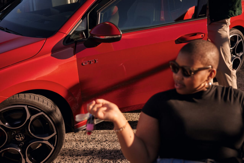 Una chica delante de un Volkswagen Golf GTI rojo