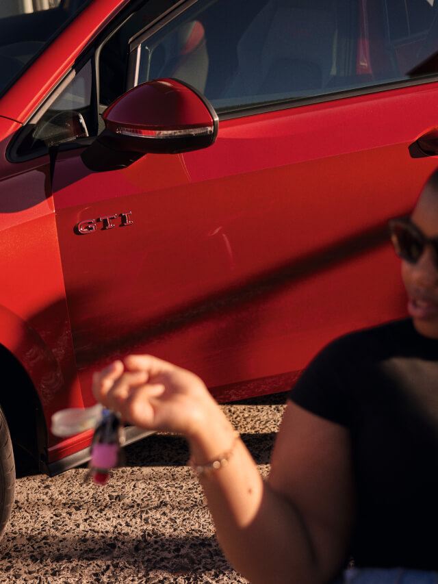 Una chica con unas llaves en la mano delante de un Volkswagen Golf GTI de color rojo