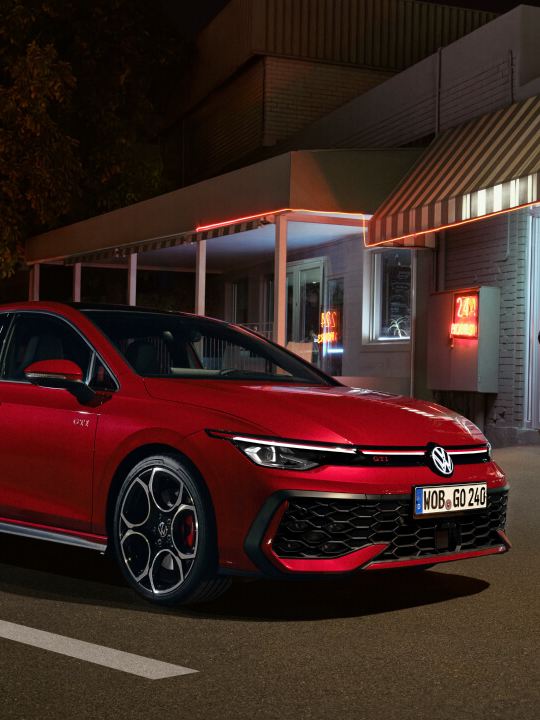 Un Volkswagen GTI de color rojo estacionado fuera de un establecimiento por la noche