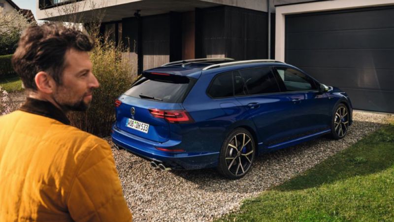 Un Volkswagen Golf Variant R azul aparcado en una casa con un hombre en primer polano