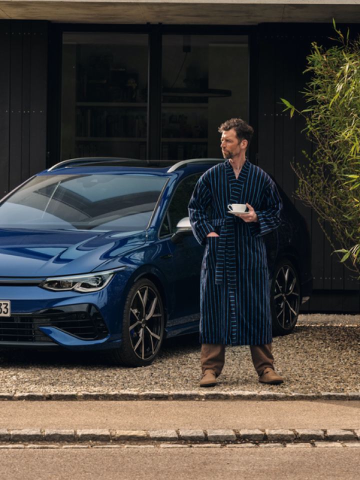 Mujer hombre de pie delante de un Volkswagen Golf 8 Variant R azul aparcado en una casa