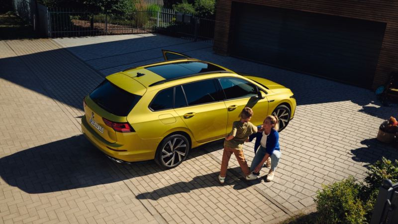 Madre con su hijo con un Volkswagen Golf Variant amarillo aparcado en casa
