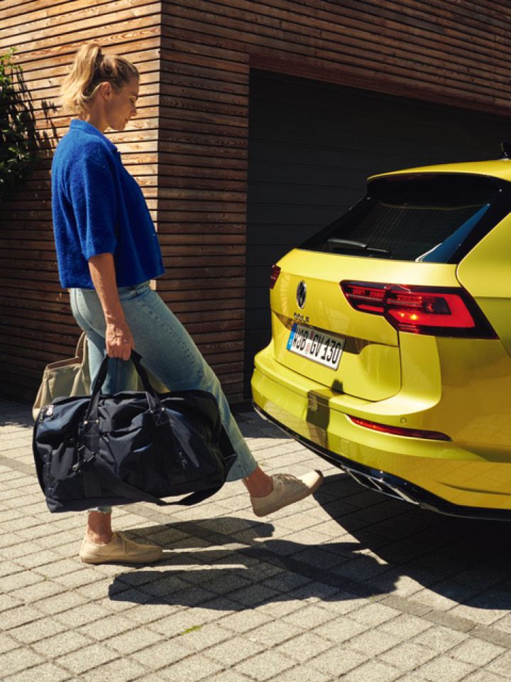 Mujer con maletas abriendo con el pie el portón trasero del Volkswagen Golf 8 Variant