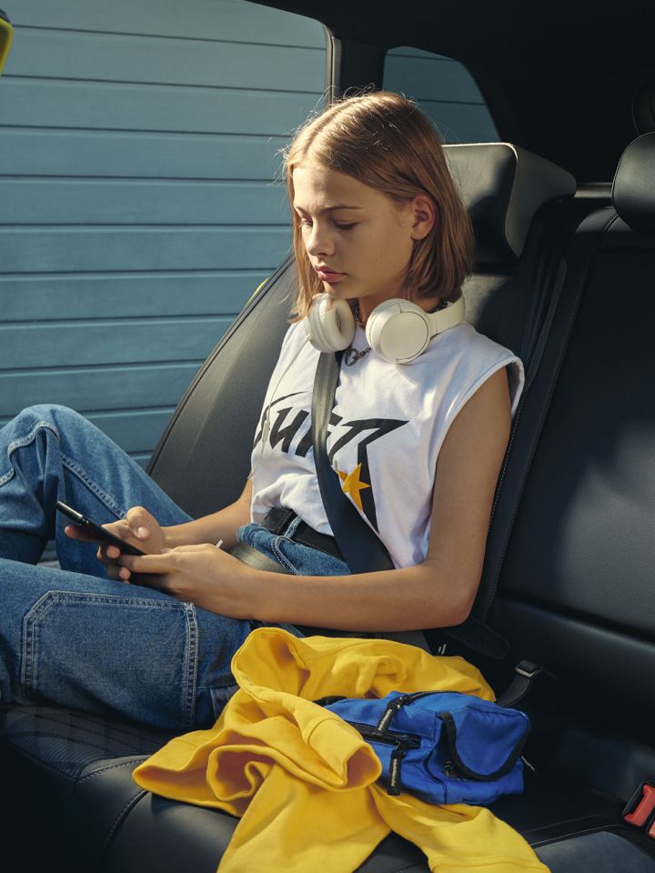 Una chica con un móvil y auriculares sentada en la parte trasera de un Volkswagen Golf 8 Variant