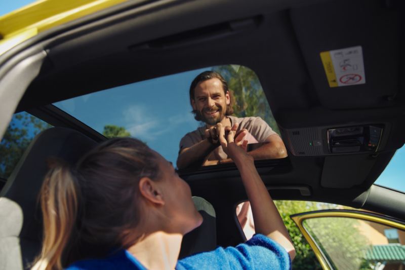 Chica sentada en un Volkswagen Golf 8 Variant mirando a un chico a través del techo solar