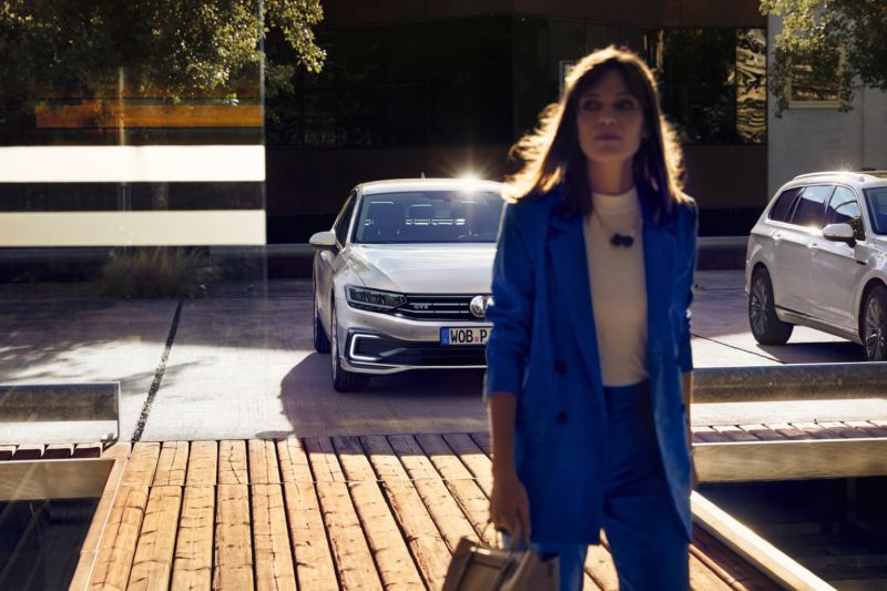 Chica en primer plano delante de un Volkswagen Passat Variant GTE aparcado visto de frente