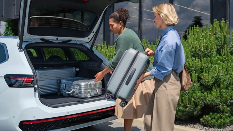 dos mujeres introduciendo dos maletas en el maletero de un Volkswagen Passat blanco