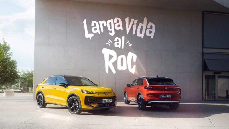 Un Nuevo Volkswaqgen T-Roc rojo y otro amarillo delante de un muro con un grafiti que dice "Larga vida al Roc"