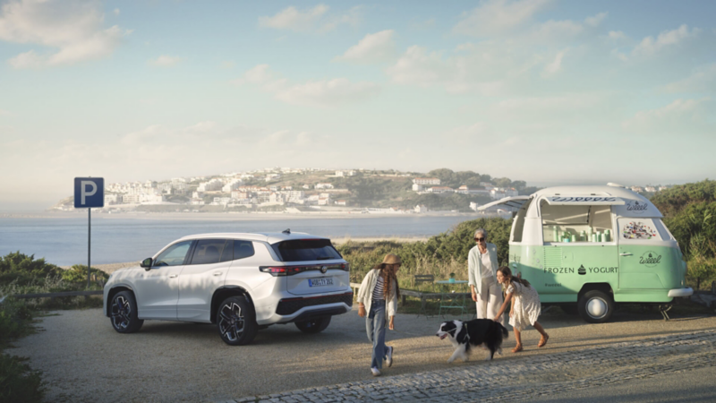 Familia con un perro frente a un Volkswagen Tayron aparcado en la playa